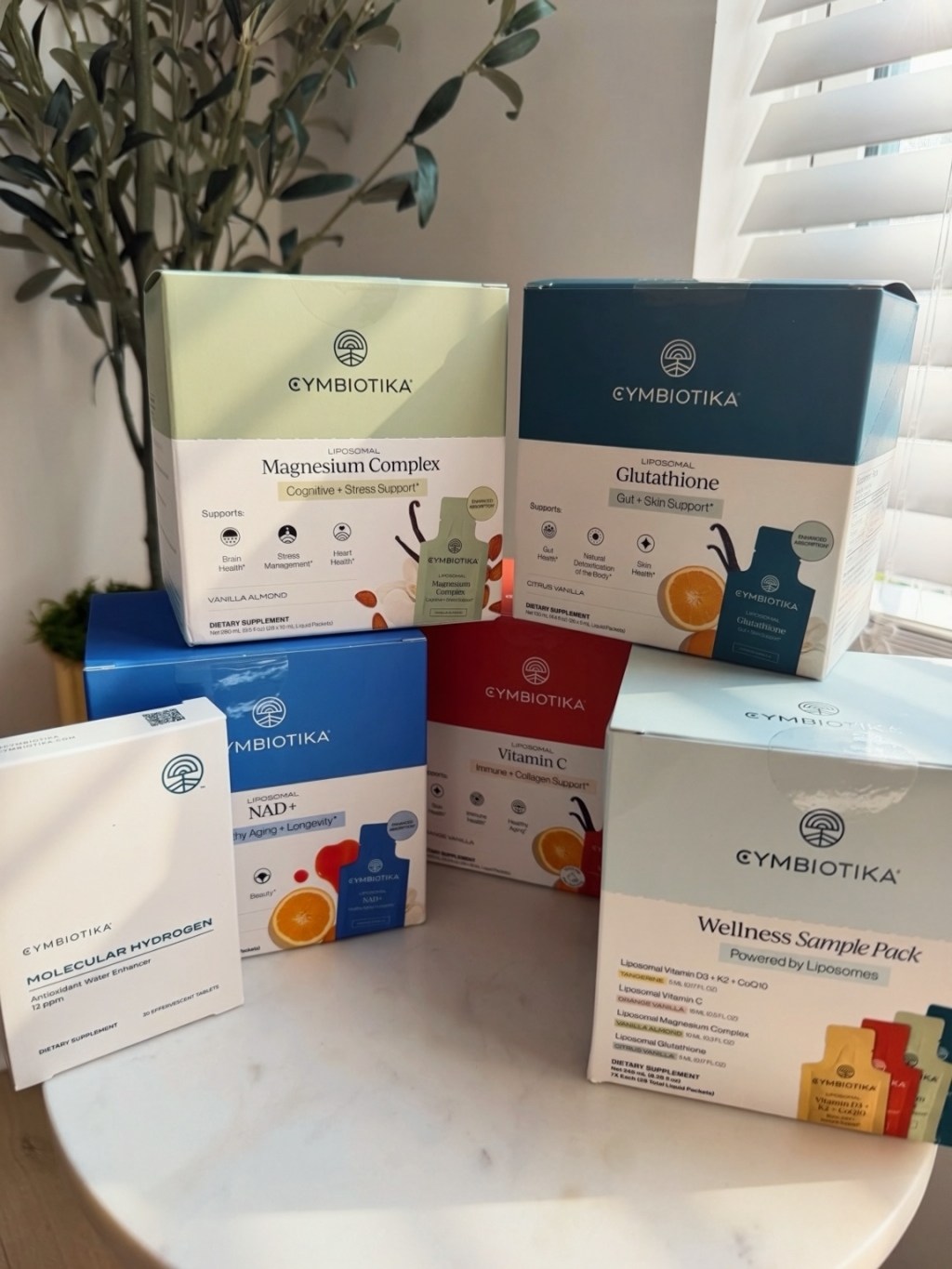 Cymbiotika liposomal supplements and Wellness Sample Pack arranged together on a sunlit kitchen counter.