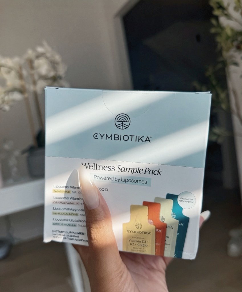 A hand holding the Cymbiotika Wellness Sample Pack in soft window light.